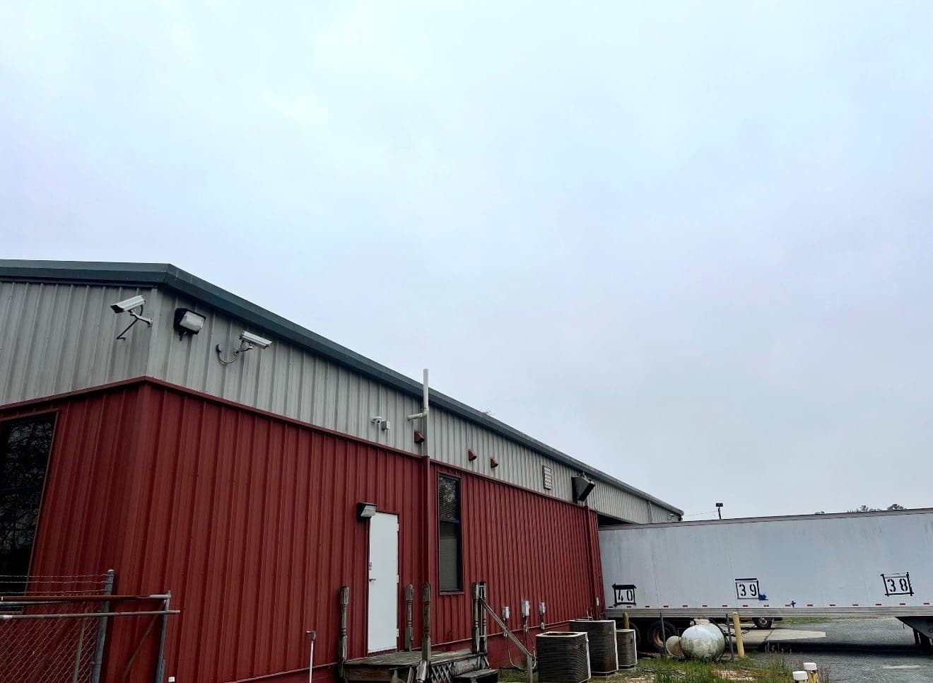 Commercial metal building with weathered red walls and a gray roof line before repainting